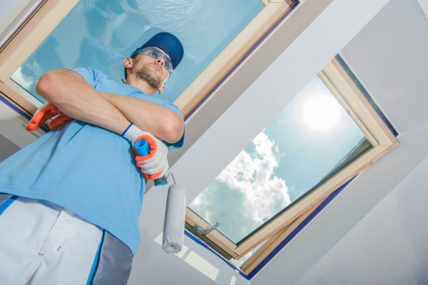 Caucasian Painter at His 40s Proudly Standing in Front of Freshly Painted Room in Residential Building with Paint Roller in His Hand. Satisfaction after a well done job.