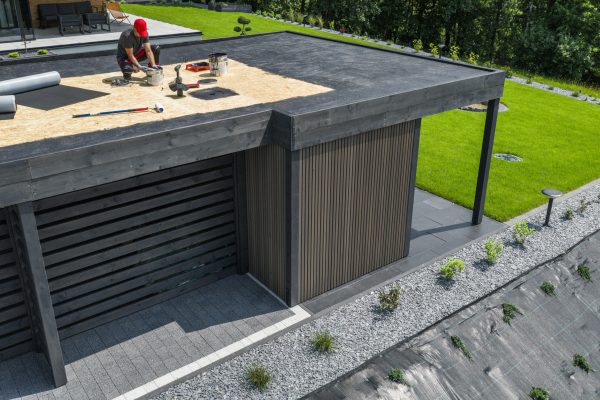 Skilled workers are completing maintenance tasks on the roof of a contemporary building, with lush greenery nearby and tools scattered around.